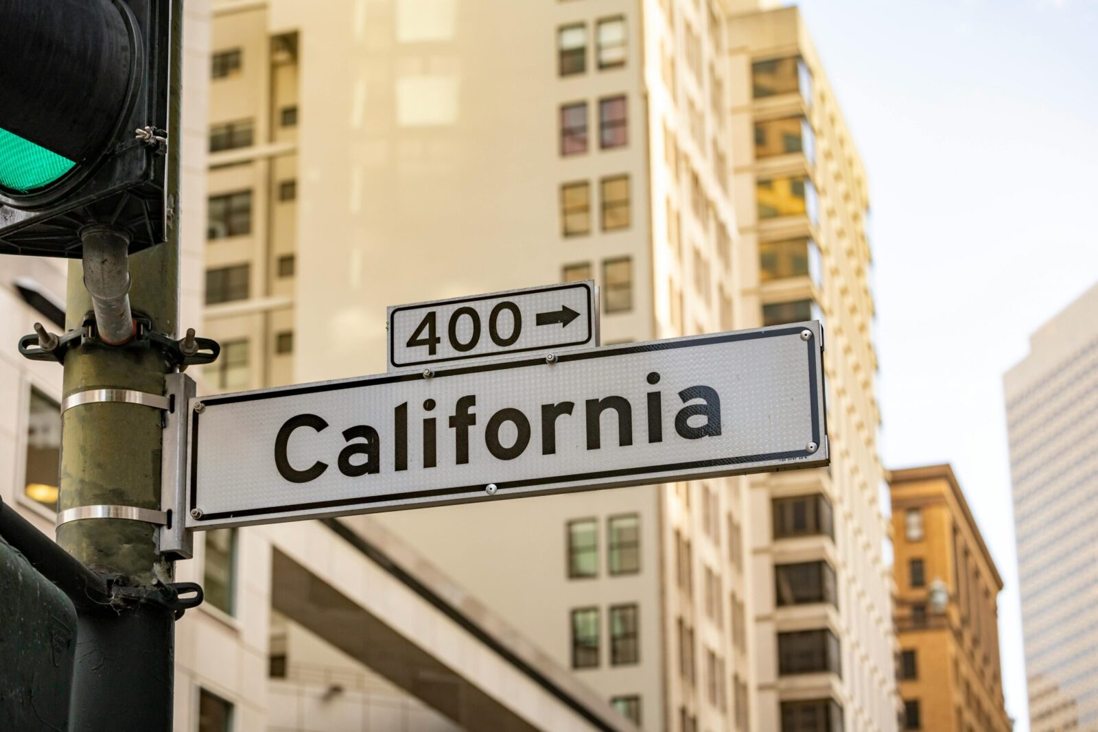 Street sign of California in an urban landscape featuring tall buildings and a traffic light.