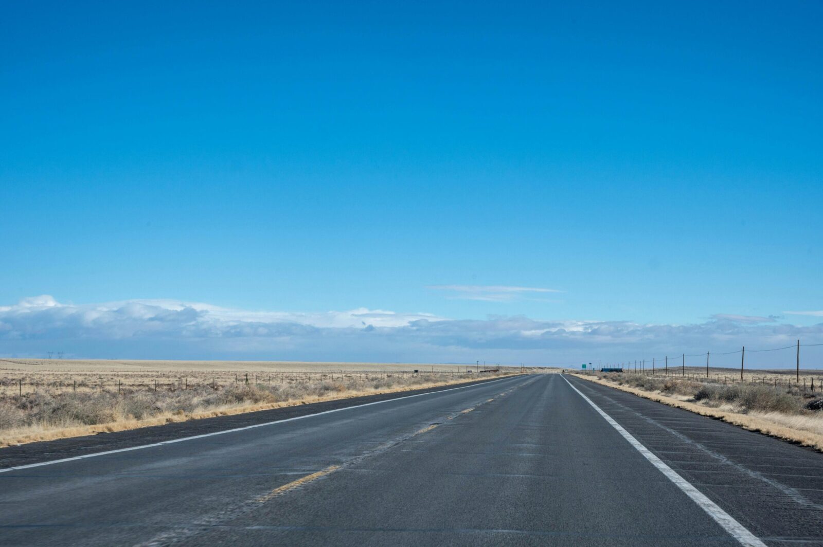 A long empty highway stretching through a vast desert terrain under a clear blue sky.