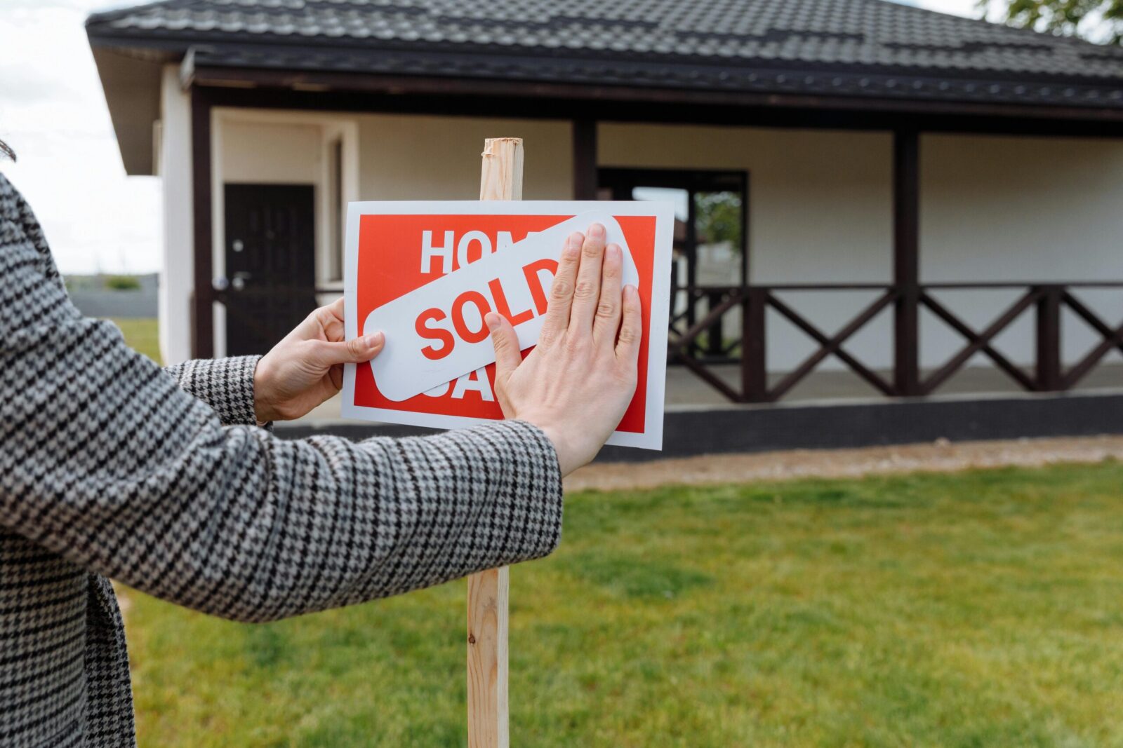 Close-up of hands placing 'sold' sticker on sign in front of a new house.