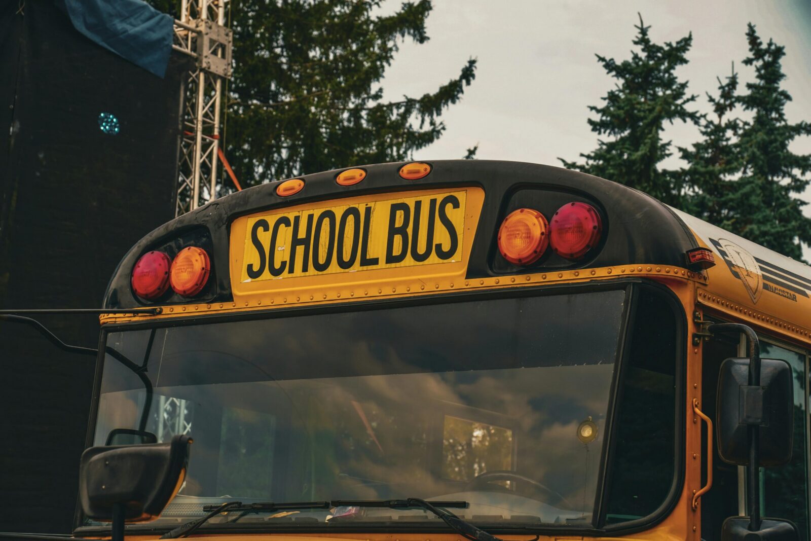 Yellow school bus outdoors in Kyiv, Ukraine, with trees and metal structures in background.