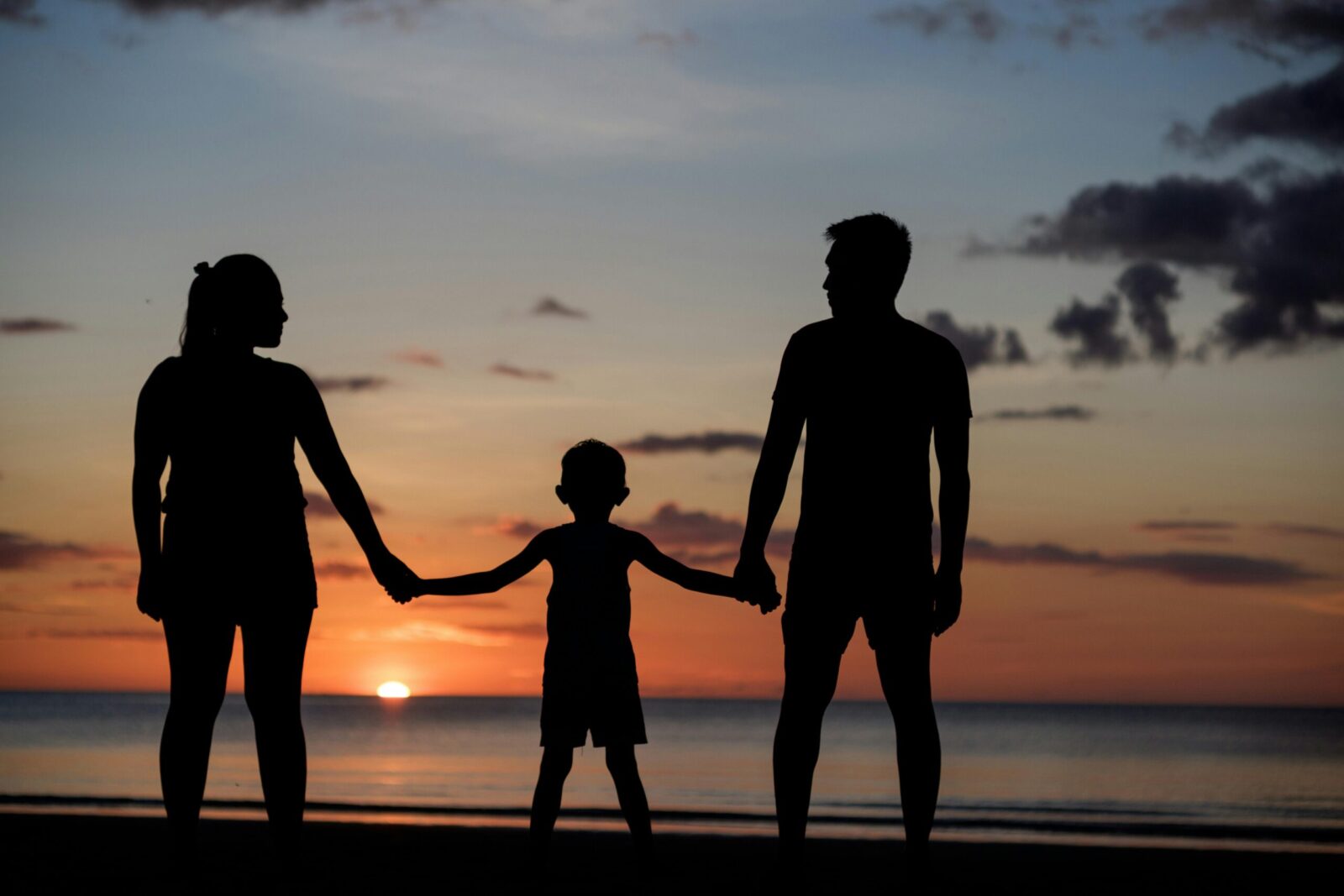 A silhouette of a family holding hands on a beach during a beautiful sunset.
