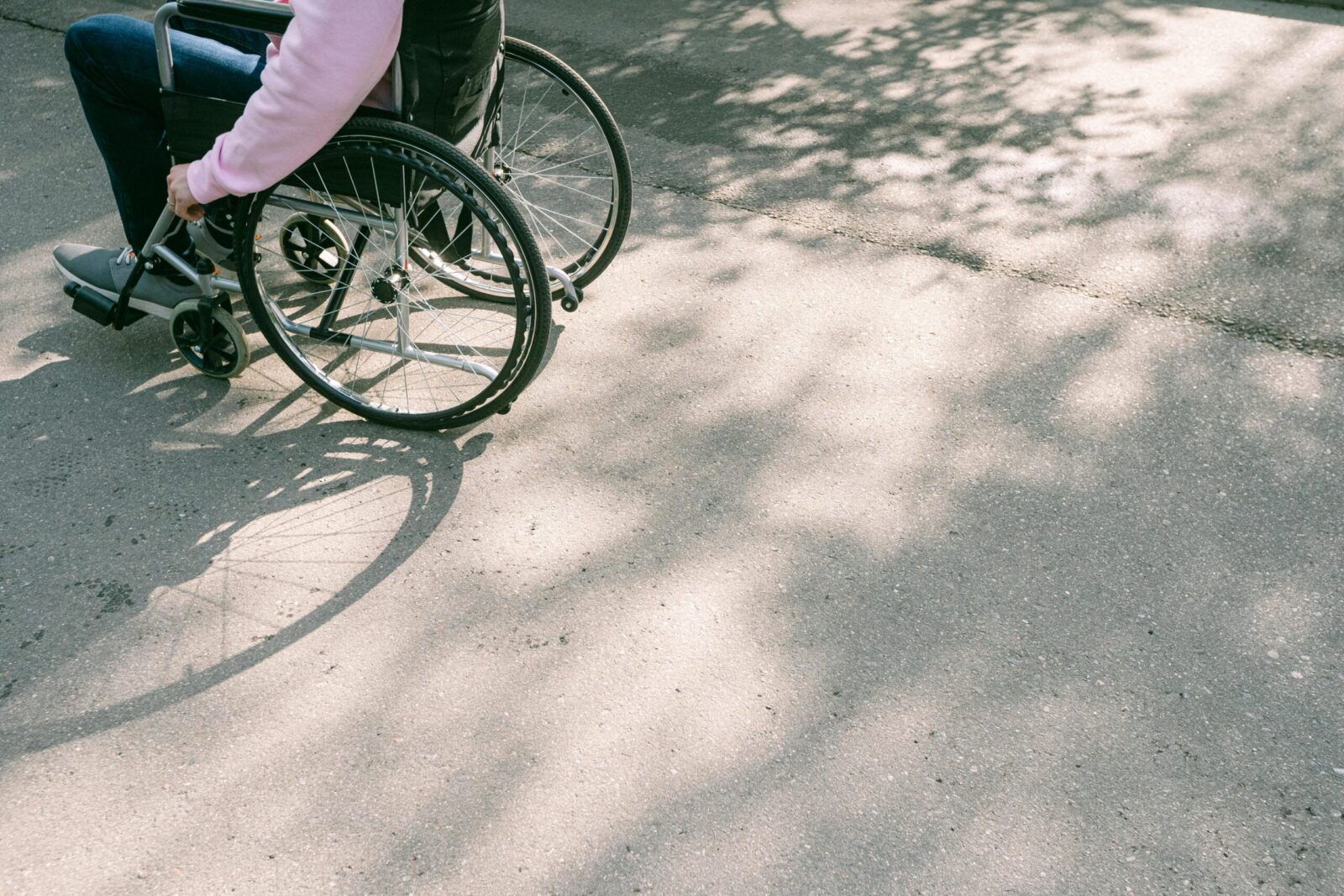 A person in a wheelchair navigating a sunlit road with tree shadows. The image captures a moment of mobility and independence.