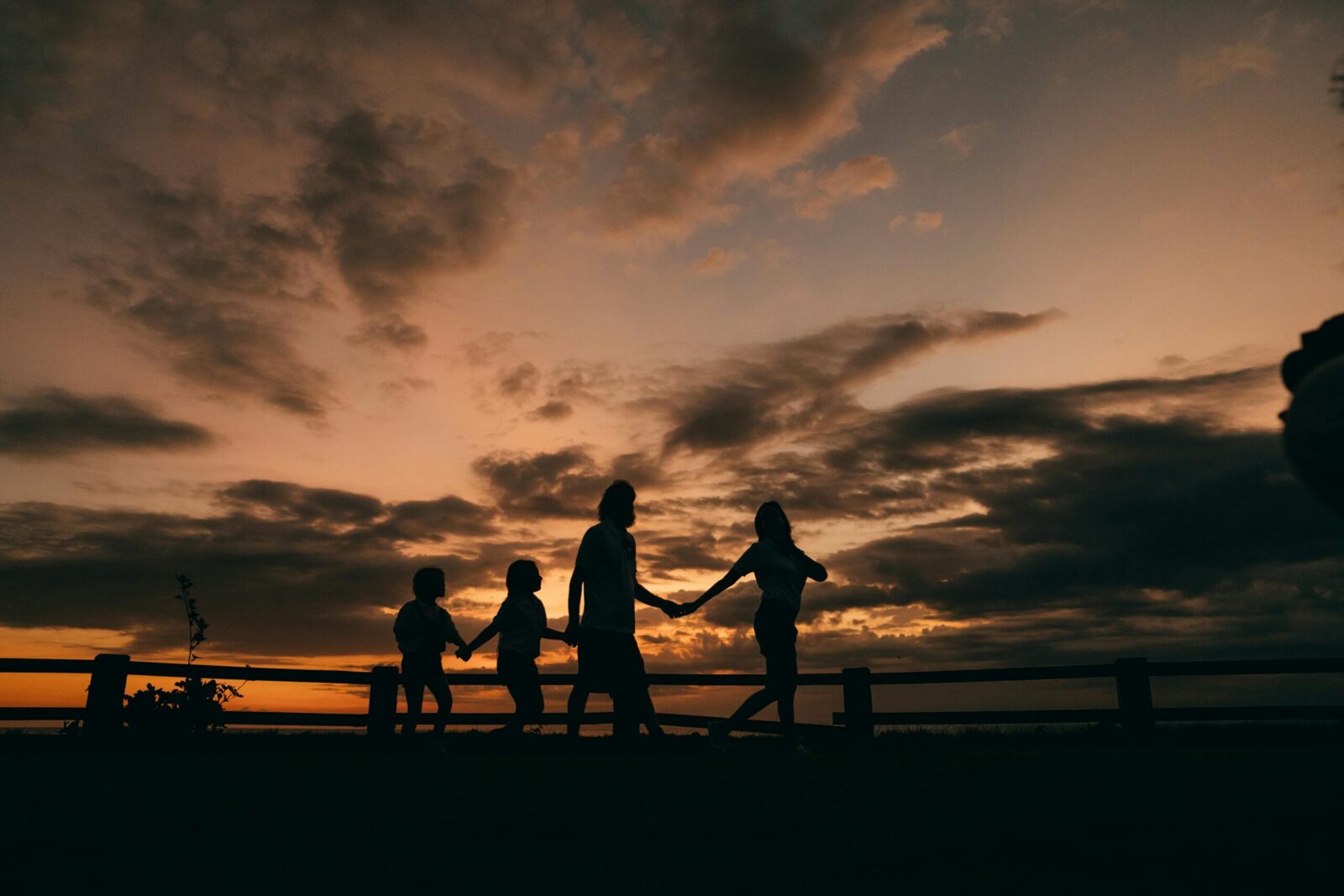 A family holding hands and walking in silhouette against a stunning sunset sky.