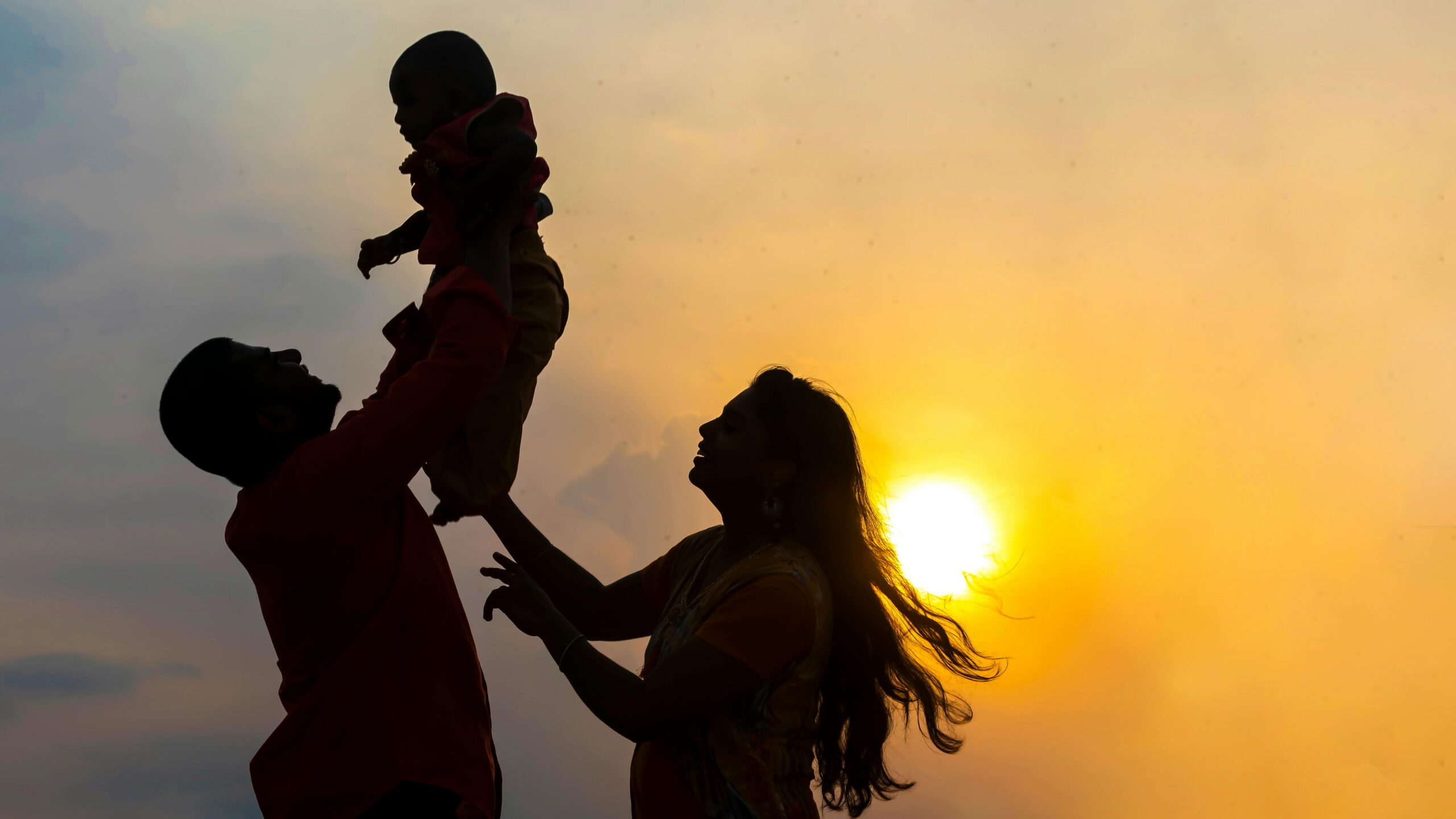 A family shares a joyful moment silhouetted against a vibrant sunset in Chennai, India.