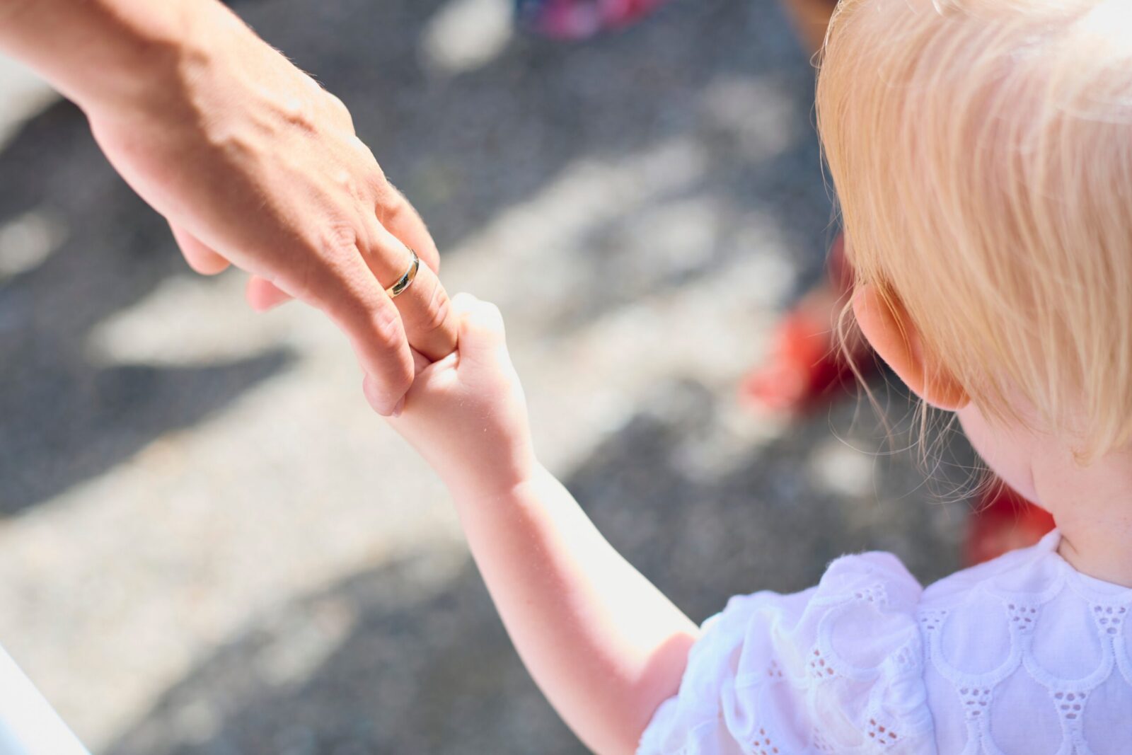 Blonde child holding parent's hand outdoors, symbolizing love and protection.