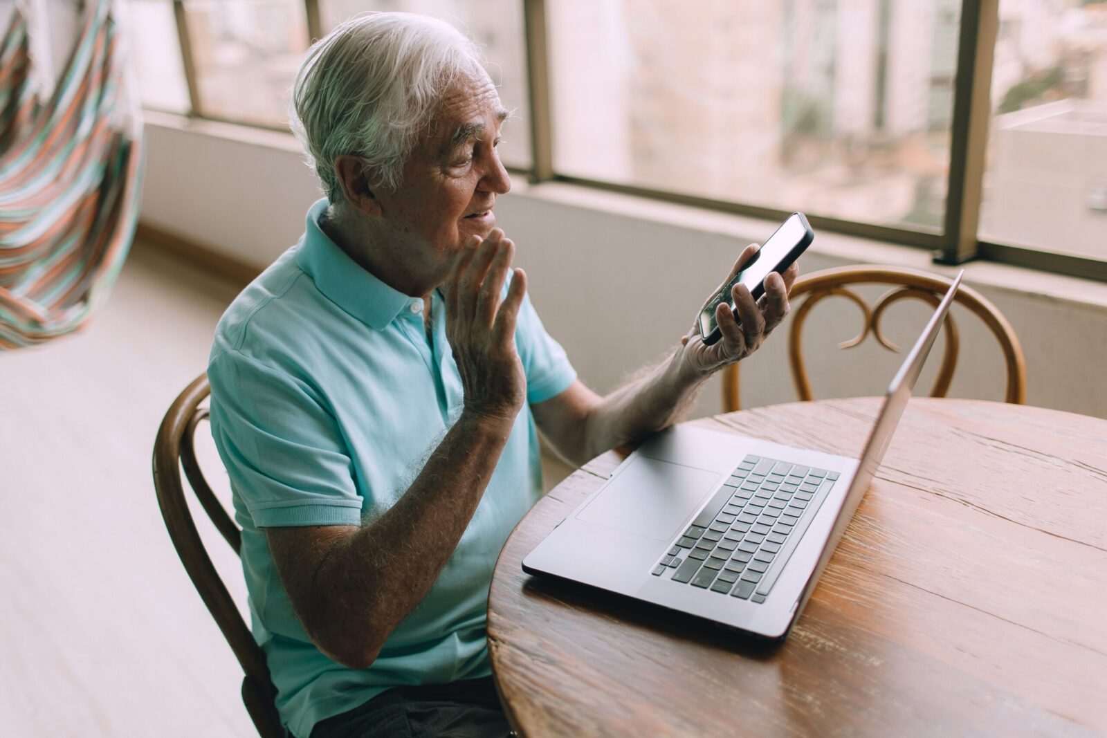 Senior man engaging in a video call using smartphone and laptop indoors.