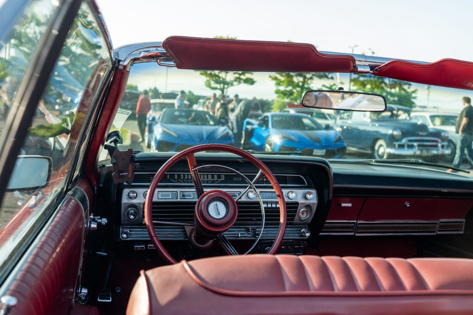 A vintage car interior view at an outdoor auto show featuring classic cars in the background.