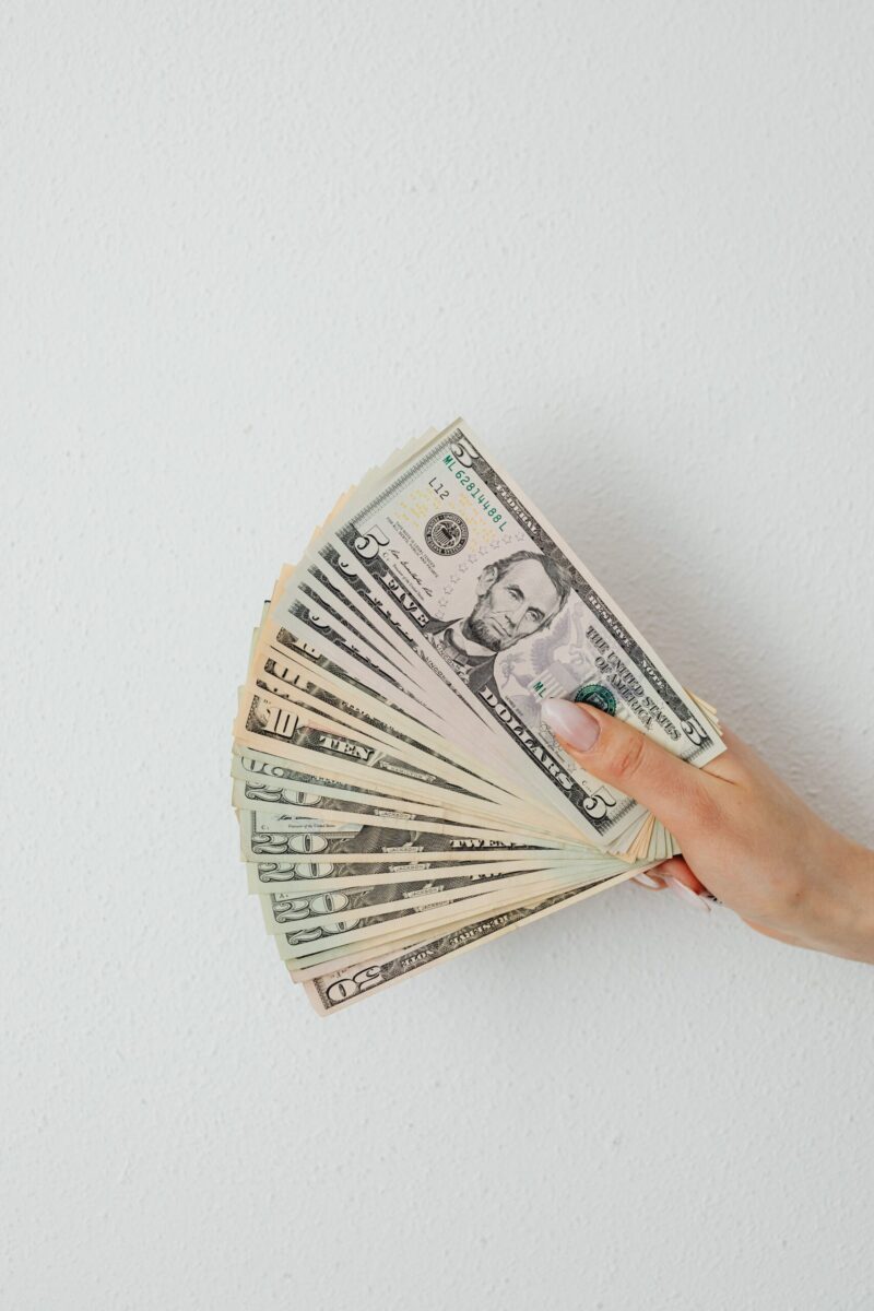 Close-up of a hand holding a fan of US dollar bills against a white surface.