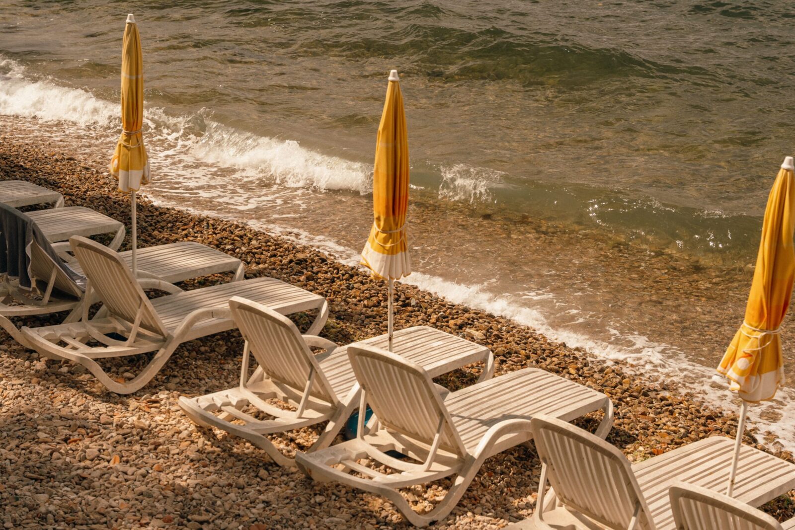 Serene pebble beach with sunbeds and umbrellas, captured during a golden summer sunset.