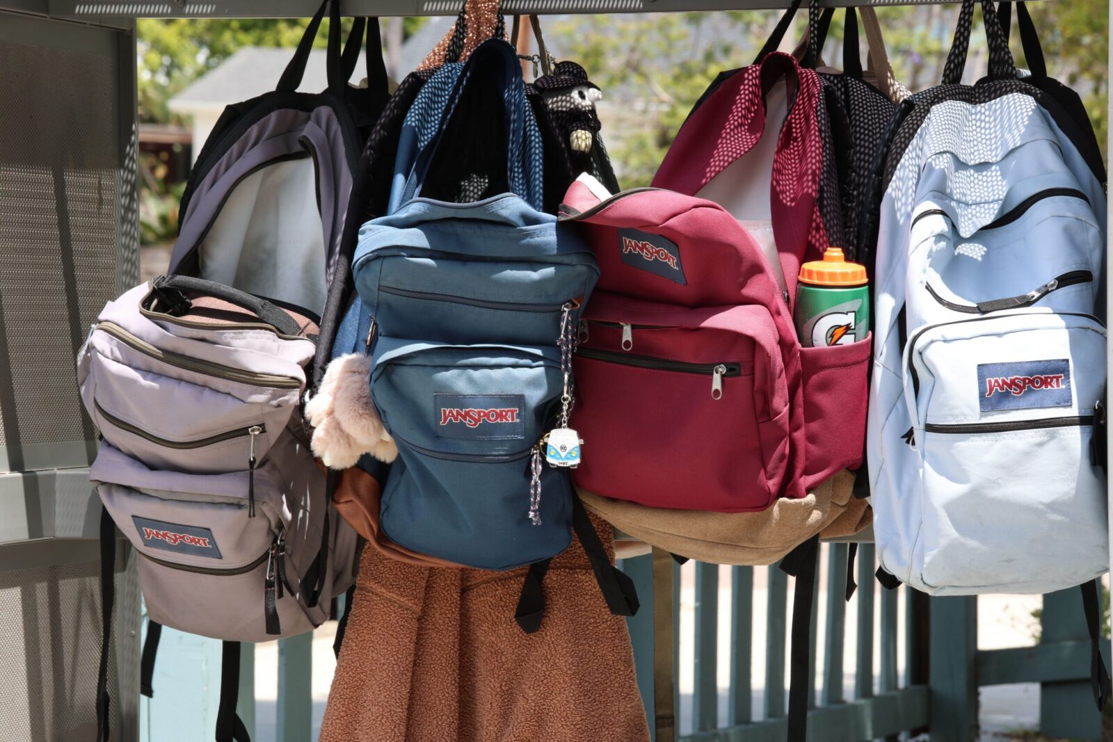 A collection of colorful backpacks hanging outside on a sunny day. Perfect for back-to-school themes.