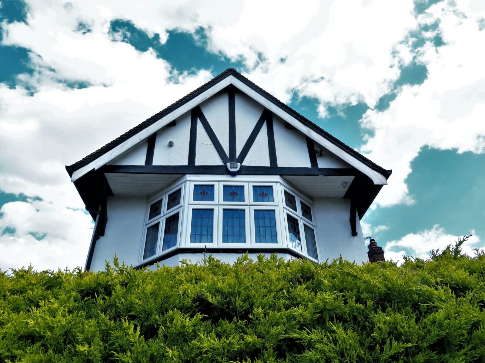 Tudor-style house facade with a bay window against a vibrant sky and greenery.
