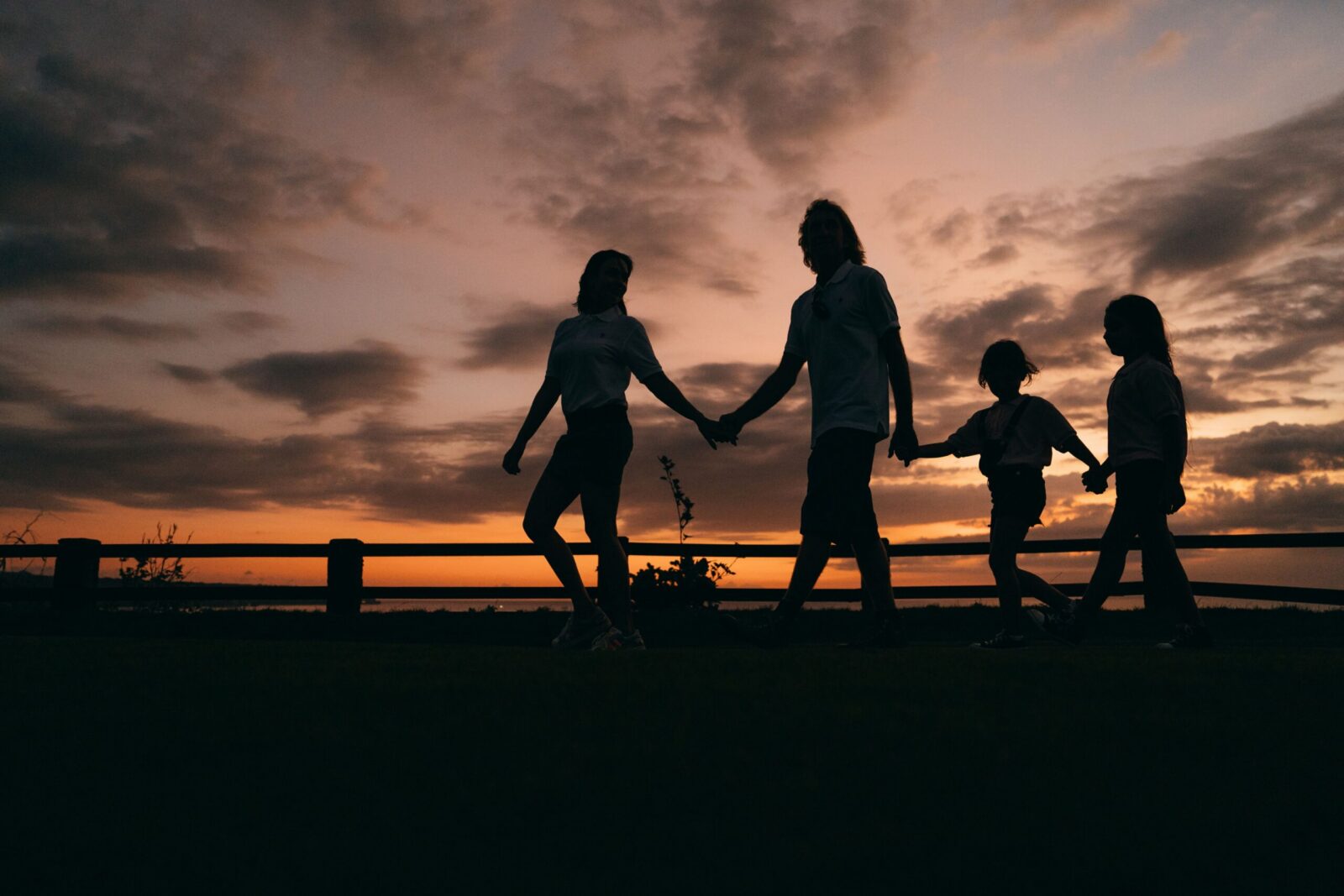 A family walks hand in hand against a vibrant sunset, evoking togetherness and peace.